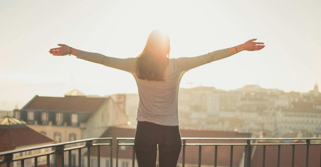 A woman stands with outstretched arms on a sunny balcony, embracing the morning light.