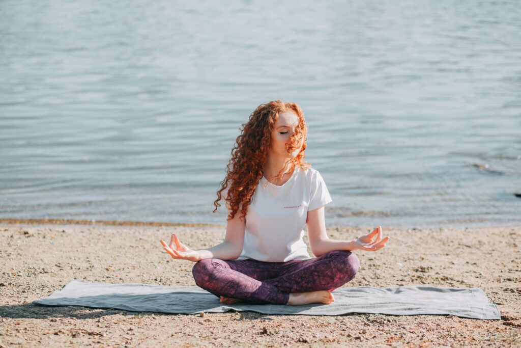 A serene image of a woman practicing yoga on a sunlit beach by the ocean.